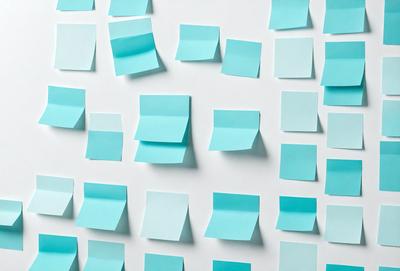 The primary subject of the image is a wall covered with blue sticky notes. The setting is a white wall, and the visual style is a photo. The dominant colors are blue and white, creating a calm and organized atmosphere.