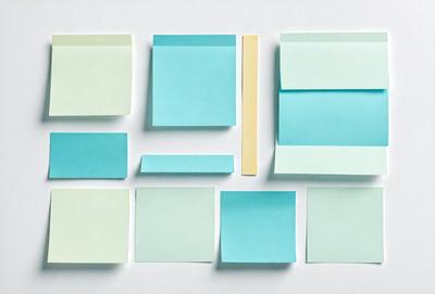 The primary subject of the image is a collection of different colored sticky notes. The setting is a white surface, and the visual style appears to be a photo. The colors and mood of the image are predominantly blue and green, giving it a calm and organized appearance.