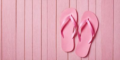 The primary subject of the image is a pair of pink flip flops. The setting is a pink wall, which serves as the backdrop for the flip flops. The visual style is a photo, capturing the flip flops in their natural environment. The colors and mood of the image are predominantly pink, creating a warm and inviting atmosphere.