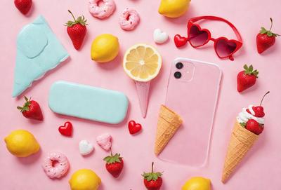 The primary subject of the image is a pink cell phone with a pink case, placed on a pink surface. The setting is a pink background, and the visual style is a photo. The dominant colors are pink and yellow, creating a warm and cheerful atmosphere.