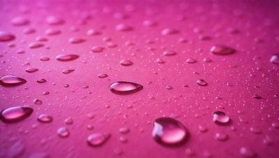 The primary subject of the image is a close-up of a pink surface with water droplets on it. The surface appears to be a piece of fabric or a piece of pink paper. The setting is a room with a pink background. The visual style is a close-up of the pink surface with water droplets. The colors and mood of the image are predominantly pink, giving it a warm and inviting atmosphere.
