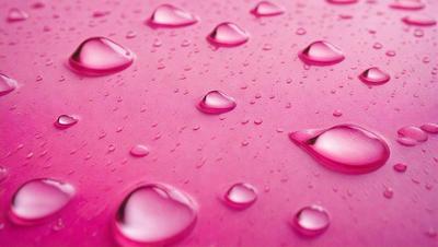 The primary subject of the image is a close-up of a pink surface with water droplets on it. The surface appears to be a pink fabric or a pink background. The visual style of the image is a close-up, which emphasizes the details of the water droplets. The colors and mood of the image are predominantly pink, creating a warm and inviting atmosphere.