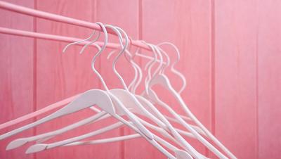 The primary subject of the image is a white hanger with multiple white hangers hanging on it. The hangers are arranged in a row, and they are all white. The setting is a pink wall, which provides a contrasting background to the white hangers. The visual style of the image is a close-up of the hangers, showcasing their details and arrangement. The colors and mood of the image are predominantly white and pink, creating a clean and fresh atmosphere.