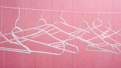 The primary subject of the image is a row of white hangers hanging on a pink wall. The hangers are arranged in a neat line, and they are all the same size and shape. The setting is a room with a pink wall, and the visual style is a realistic representation of the scene. The colors and mood of the image are predominantly pink, creating a warm and inviting atmosphere.