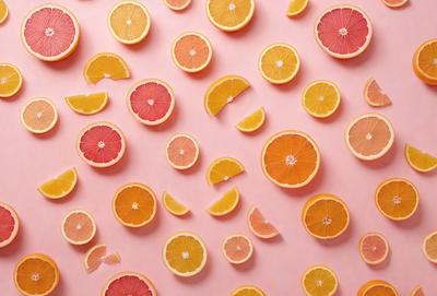 The primary subject of the image is a large number of orange slices arranged on a pink background. The slices are cut into various shapes and sizes, creating a visually appealing pattern. The setting is a pink surface, which contrasts with the vibrant orange color of the slices. The visual style is a combination of realistic and artistic elements, as the slices are presented in a creative and eye-catching manner. The dominant colors are orange and pink, creating a warm and inviting atmosphere