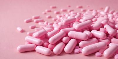 The primary subject of the image is a pile of pink pills. The setting is a pink surface, which creates a visually appealing contrast with the pills. The visual style is a close-up of the pills, showcasing their color and texture. The colors and mood of the image are predominantly pink, giving it a warm and inviting atmosphere.