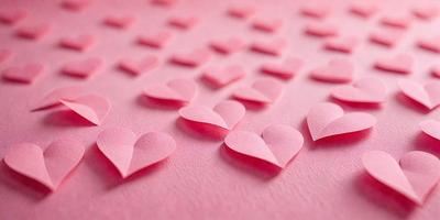The primary subject of the image is a collection of pink hearts arranged on a pink surface. The hearts are made of paper and are placed in various positions, creating a visually appealing pattern. The setting is a pink background, which complements the color of the hearts. The visual style is a combination of digital art and illustration, as the hearts are carefully arranged and the background is smooth and consistent. The colors and mood of the image are predominantly pink, creating a warm and inviting atmosphere.