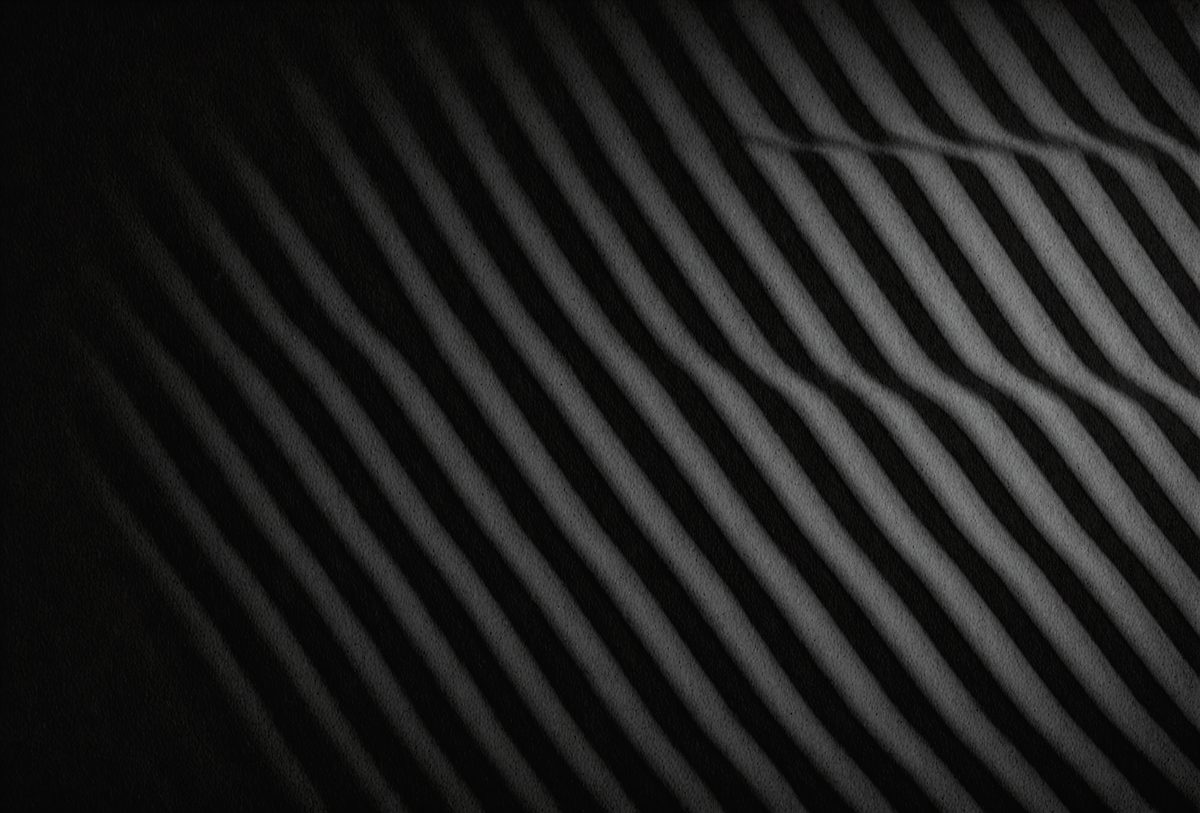 The primary subject of the image is a black and white striped pattern. The setting is a dark background, which contrasts with the pattern. The visual style is a black and white photo, giving it a classic and timeless appearance. The colors and mood of the image are predominantly dark and moody, with the contrasting light and dark stripes creating a sense of depth and intrigue.