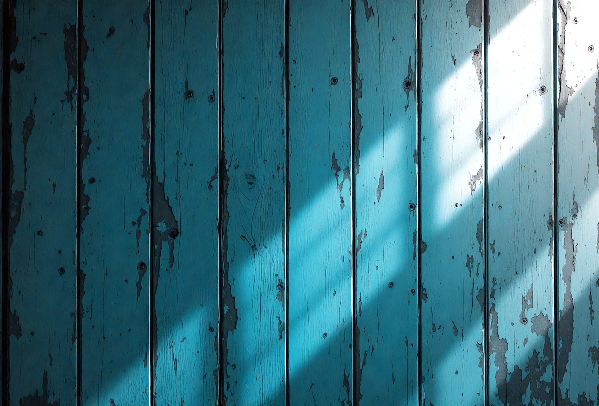 The primary subject of the image is a blue wooden wall with a peeling paint surface. The setting is a room with a window, and the visual style is a photo. The dominant colors are blue and white, and the overall atmosphere is somewhat aged and worn.