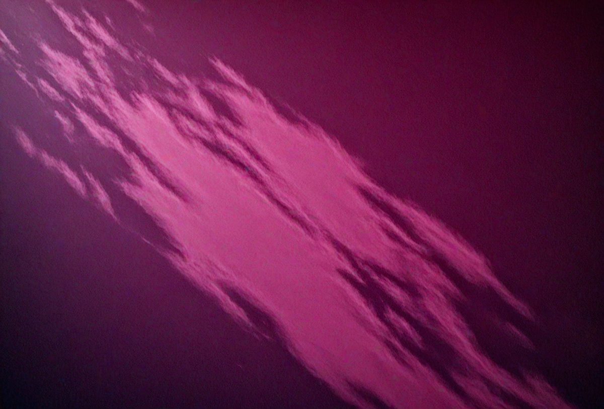 The primary subject of the image is a cloudy sky with a pink hue. The setting is a dark, cloudy sky, and the visual style appears to be a photo. The dominant colors are pink and purple, creating a moody and atmospheric scene.