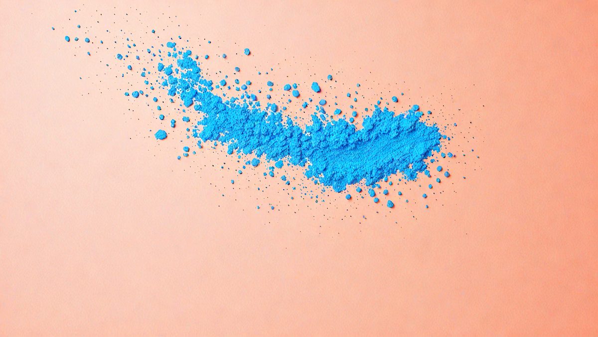 The primary subject of the image is a blue powder, which appears to be a powdered substance or a powdered food coloring. The setting is a pink surface, which could be a table or a wall. The visual style of the image is a close-up of the blue powder, showcasing its texture and color. The dominant colors in the image are blue and pink, creating a vibrant and lively atmosphere.